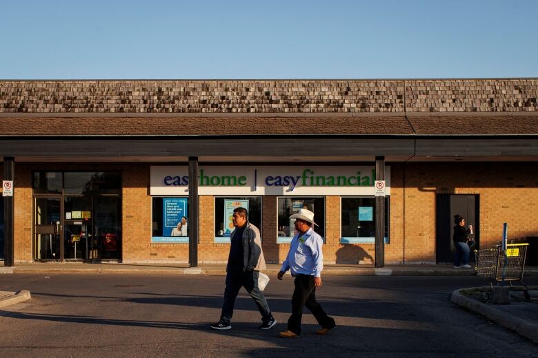 Two men walking across a parking lot at a shopping plaza.