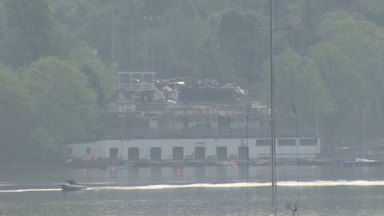 A pile of rubble that was once a large recreational club is seen across the water in the distance. A smoky haze covers the image.