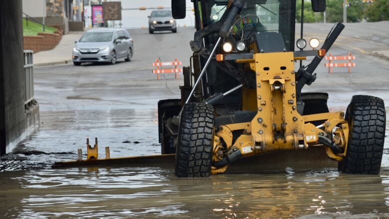 A large city vehicle is driving through a flooded area to move debris