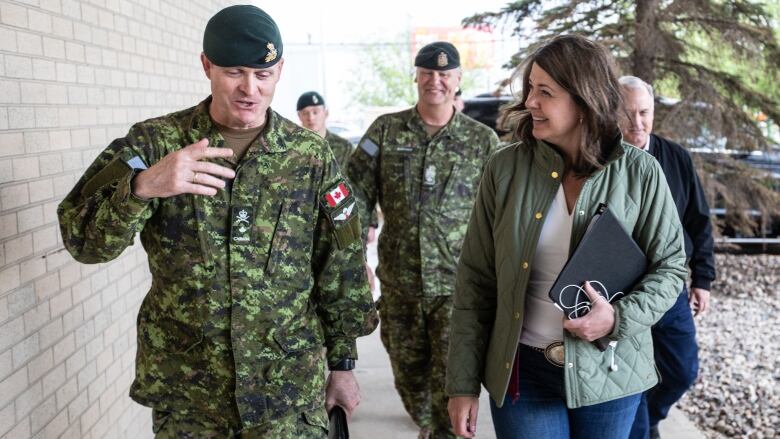 A woman and military members talk while walking.