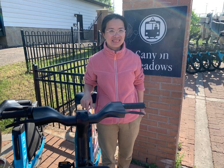 A lady smiles while standing next to an e-bike at Canyon Meadows station in Calgary. 