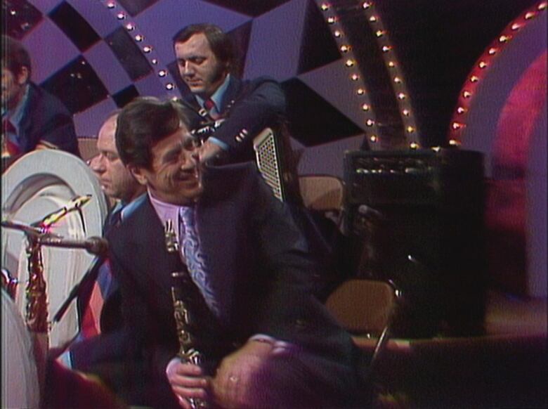 A jazz musician smiles as he holds his clarinet surrounded by his own band on television.