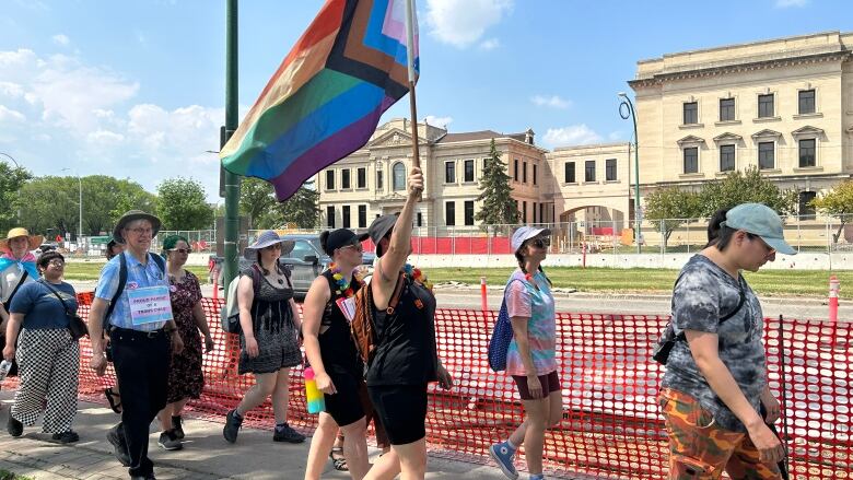 People walk down a sidewalk. One is holding up a pride flag