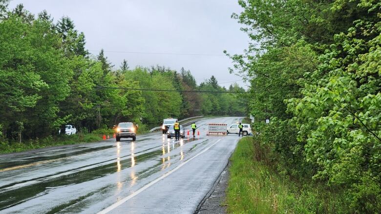 Police vehicles parked on a wet road with officers nearby and a 