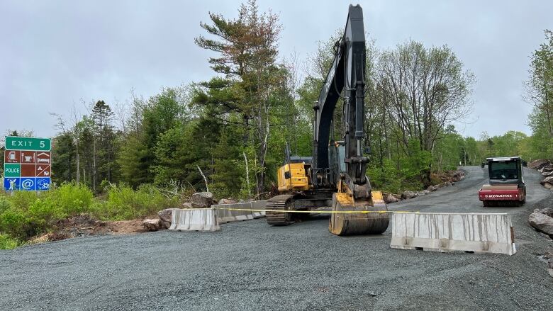 An earthmover and on a gravel clearing with a highway 103 exit sign in the background.