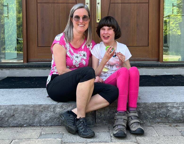 A woman and her daughter sit together on a set of steps in front of a door.