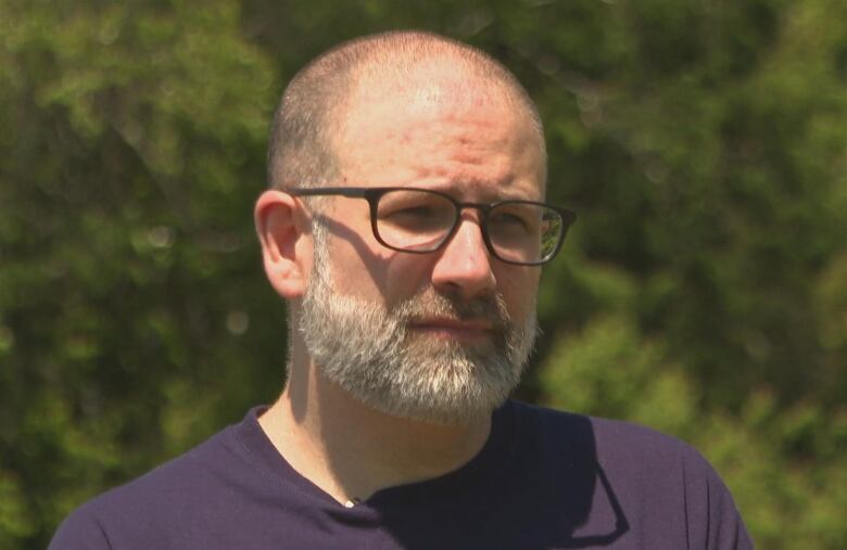 A man wearing a dark blue shirt and black-rimmed square glasses.