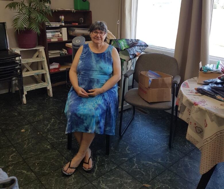 A woman wearing a blue dress can be seen sitting on a chair 