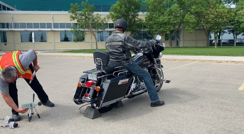 A man holds a microphone with attachments behind a Harley Davidson motorcycle