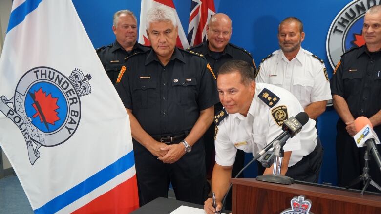 Men in official police uniforms sign an agreement around a desk. 