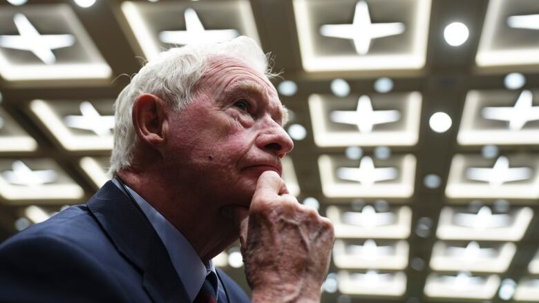 A man rubs his chin against a backdrop of ceiling lights.