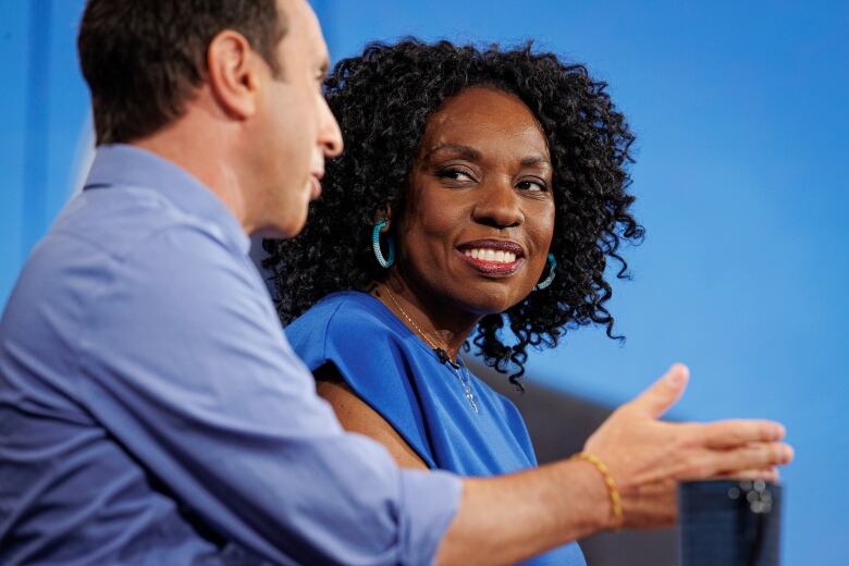 Man in a blue shirt talks beside a woman in a blue dress.