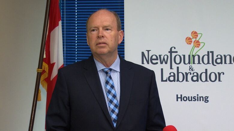 A man wearing a suit stands in front of a banner. The banner has the Newfoundland and Labrador logo on it, with the word Housing underneath.