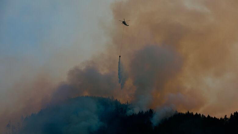 A helicopter pours water on a raging wildfire.