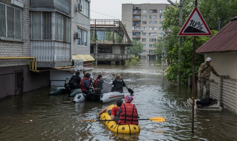 People are shown navigating inflatable boats between buildings in flooded streets of a town.