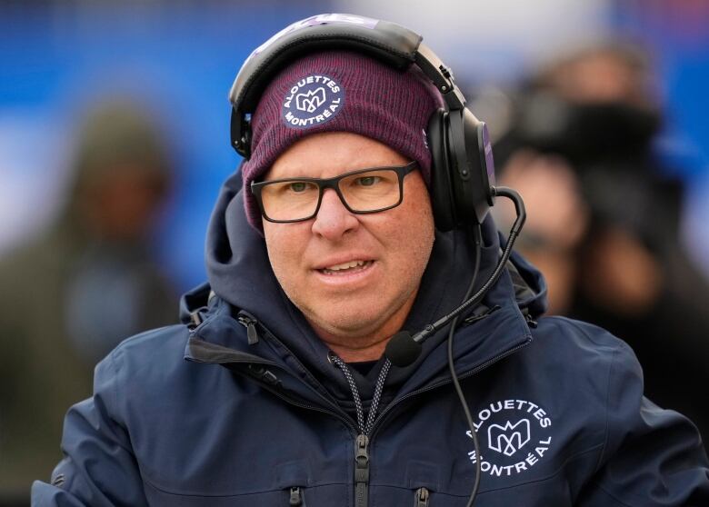 Serious-looking man with headset and mic, wearing Montreal Alouettes gear.