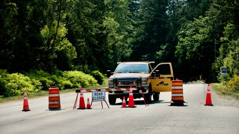 A photograph of orange cones, a road closure sign and a yellow contractor's truck barricading Highway 4.