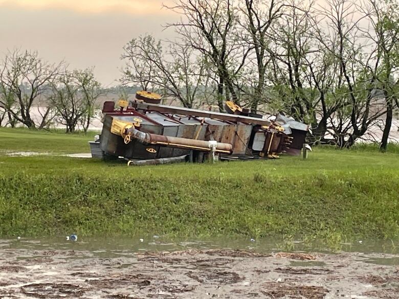 An antique piece of farm equipment is seen on its side in the middle of a green field.