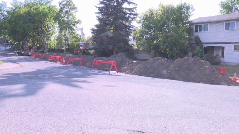 Piles of dirt sit on the roadside in a residential area. 