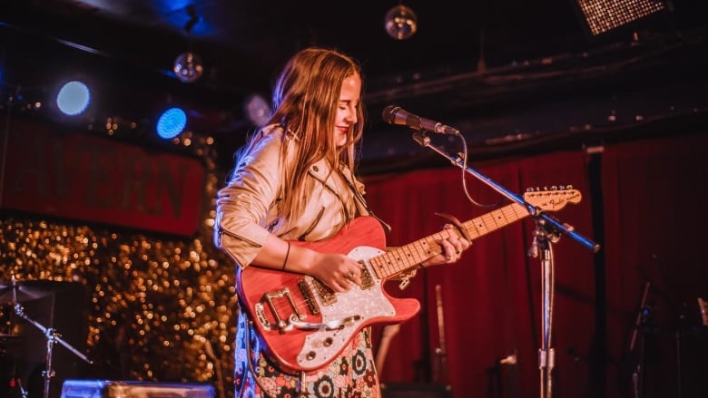 A woman plays an electric guitar in front of a microphone inside of a bar.