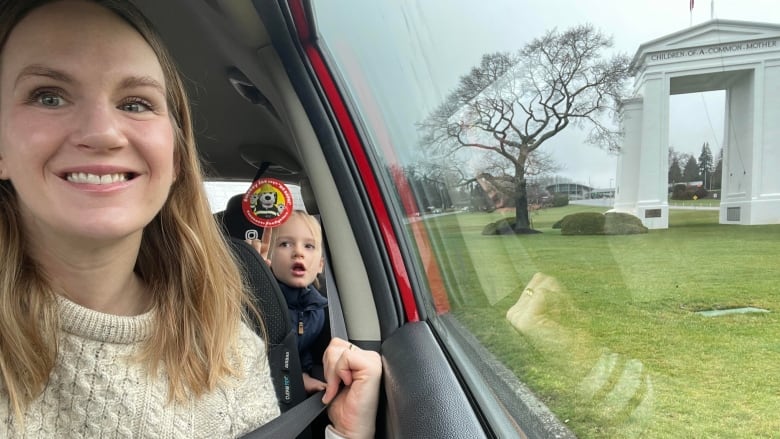 A smiling woman sits in her car with her children in the backseat in front of the Peace Arch at the Peace Arch Border Crossing.