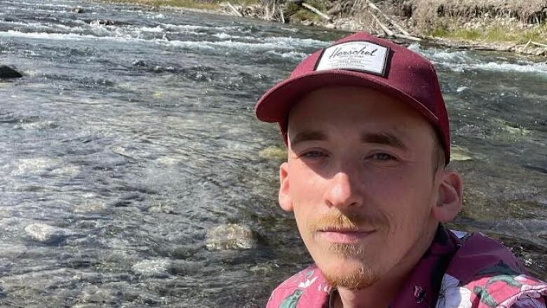 A man in a printed shirt takes a selfie in front of a clear river. 