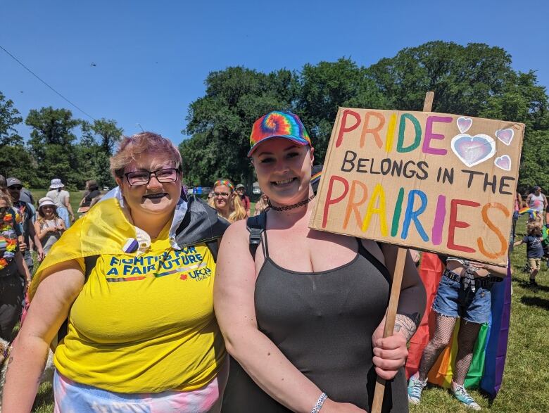 Two people stand next to each other. One holds a sign that says 