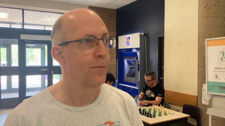 Ken stands in front of two people playing chess at Saint Mary's University in Halifax. 