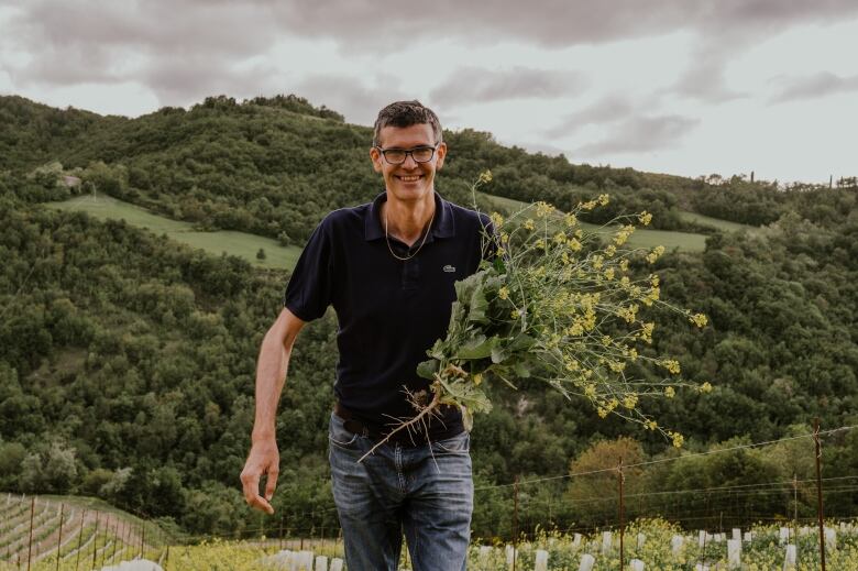 A man walks through a vineyard, holding a plant. 