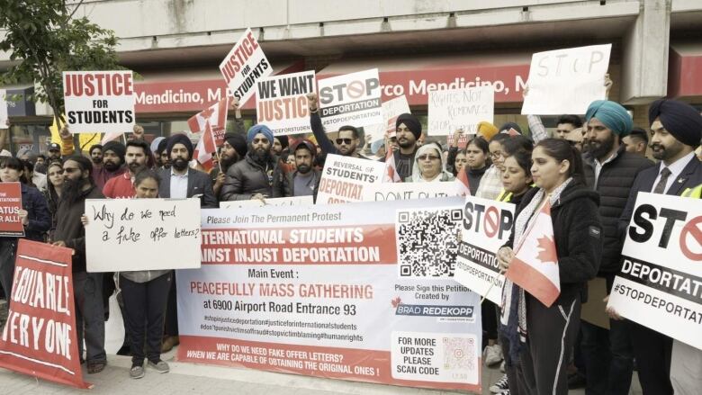 A crowd of young people of different ethnicities rally together and hold signs that say, Stop Deportation, International Students Against Unjust Deportation and Justice for Students.