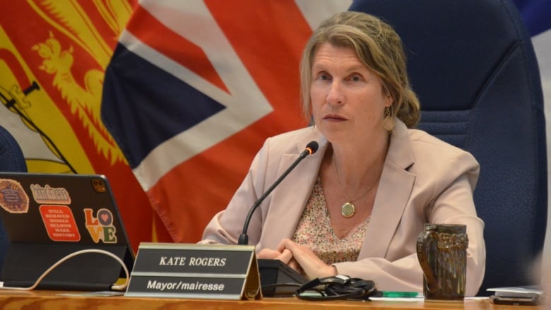 A woman sits in a chair with flags in the background.