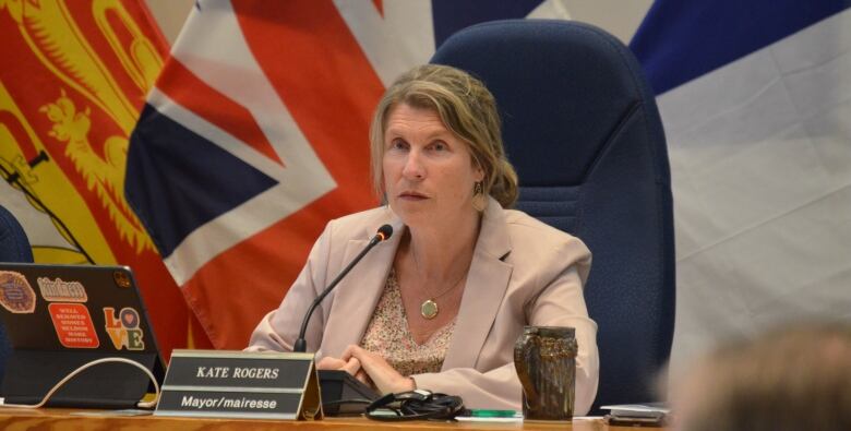 A woman sits in a chair with flags in the background.