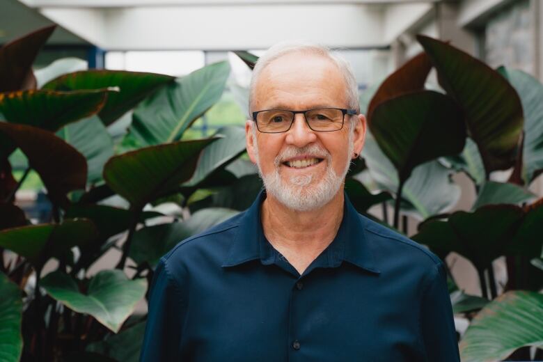 Man in blue shirt and glasses, with white beard, smiling at camera