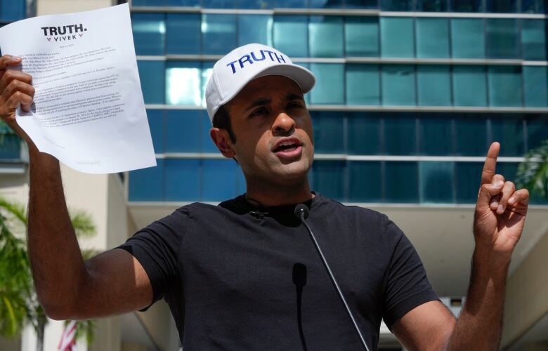 Man in cap holds up sign while talking