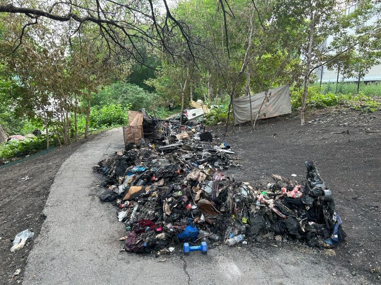 Blackened wreckage of a temporary encampment is pictured on a walking path near a river.