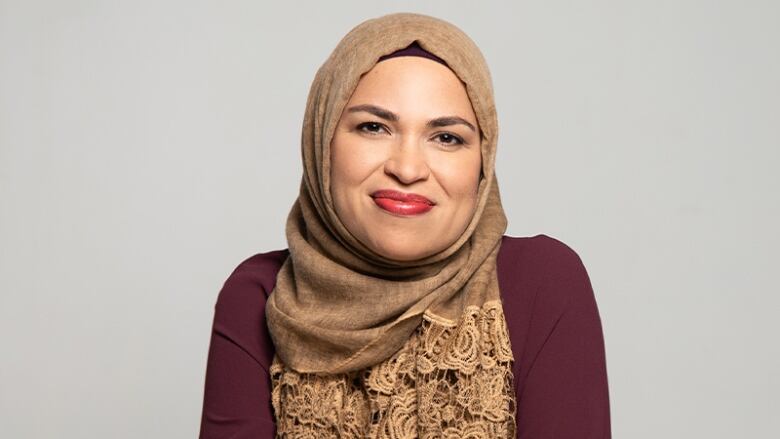 A smiling woman wearing a brown hijab sitting backwards on a folding chair.