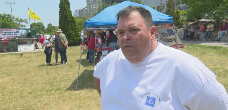 He stands outside with a blue tent and yellow flag in the background