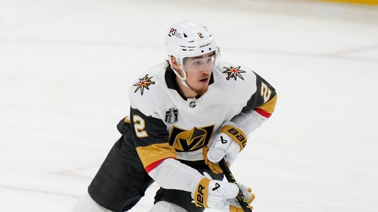 A hockey player wearing a white jersey skates on the ice.