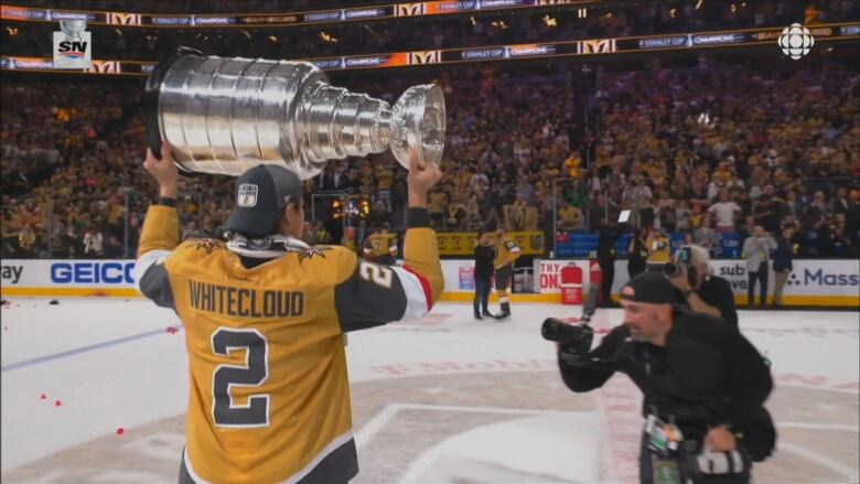 A hockey player holds up the Stanley Cup while skating on the ice.