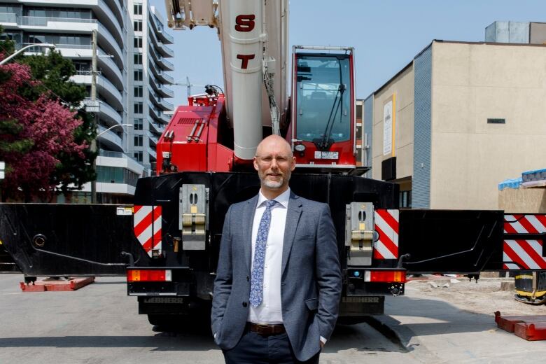 A man in a suit stands in front of a red crane.