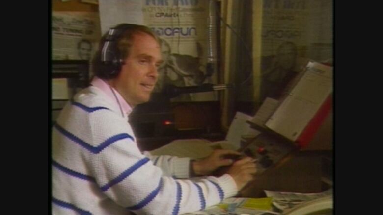 A man is wearing headphones in a radio booth with the logo 