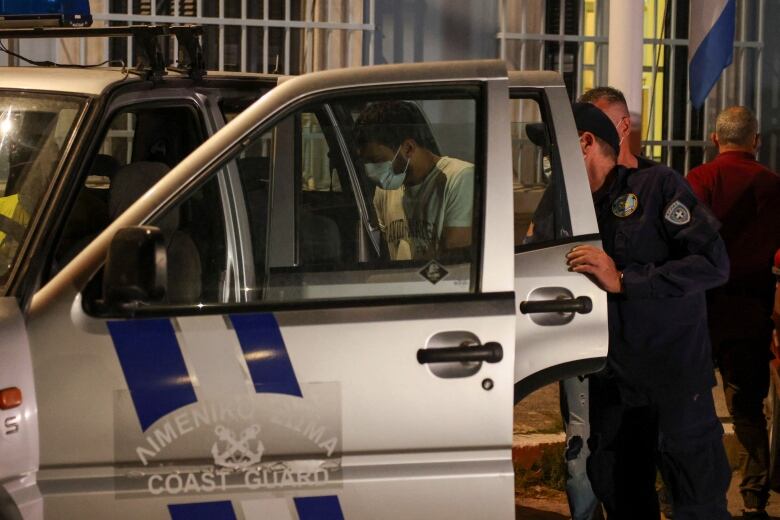 Police officers putting men into a white police vehicle