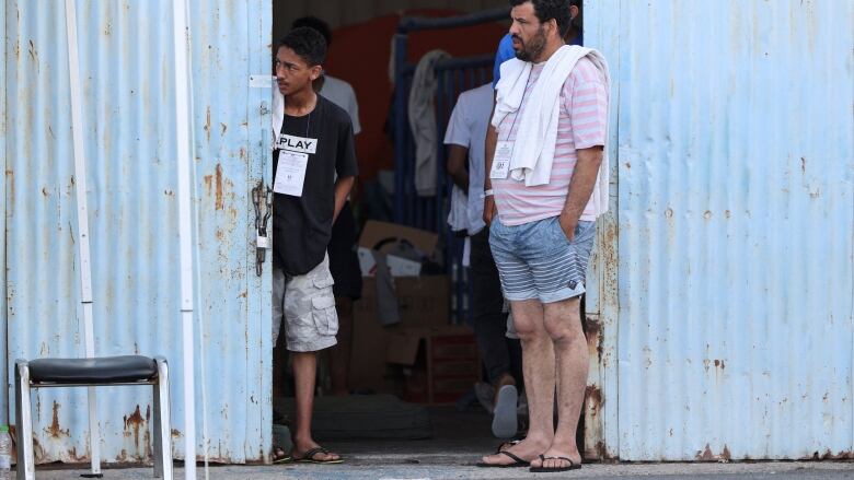 Two men standing outside a large building, looking grimly in the same direction