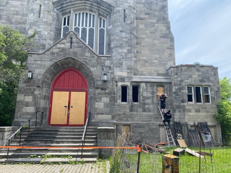 Two men make repairs to the facade of a church.