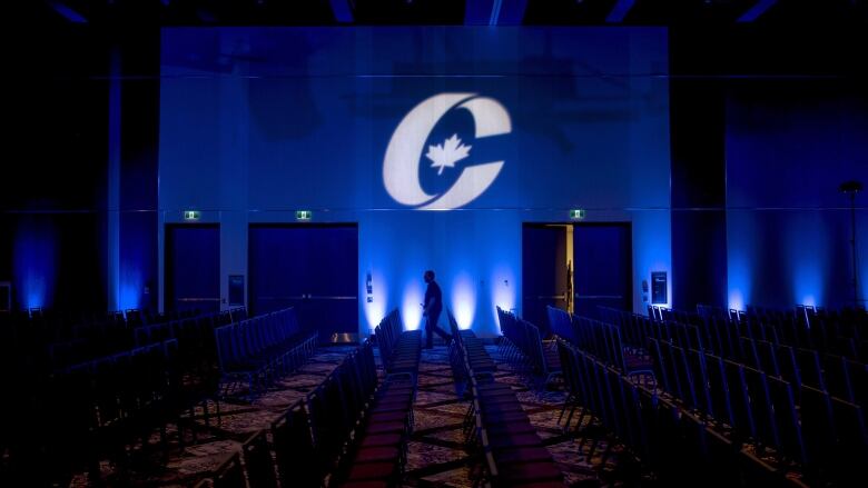 A man is silhouetted walking past a Conservative Party logo.