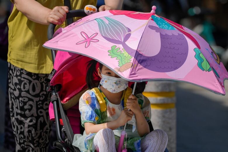 A child uses an umbrella to shield from the sun in Beijing during a heatwave in June this year.