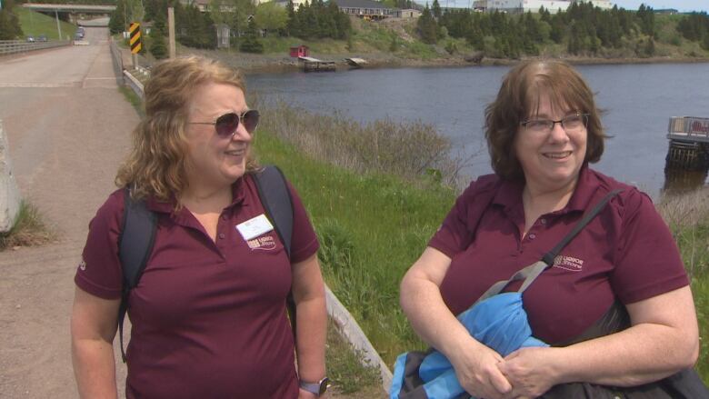 Two women wearing NLC liquor corporation shirts smile as they approach the Canning Bridge in Marystown.