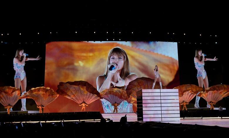 A woman with long blond hair sings into a microphone on a stage.