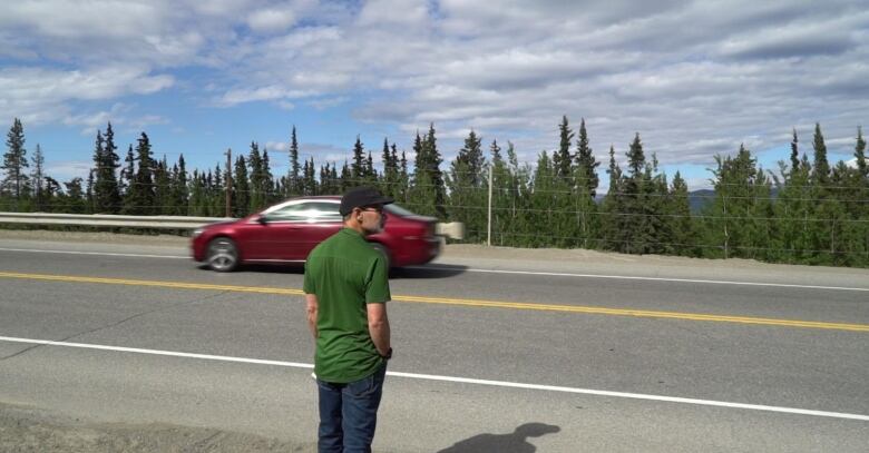 A man wearing a green shirt is crossing the Alaska Highway.