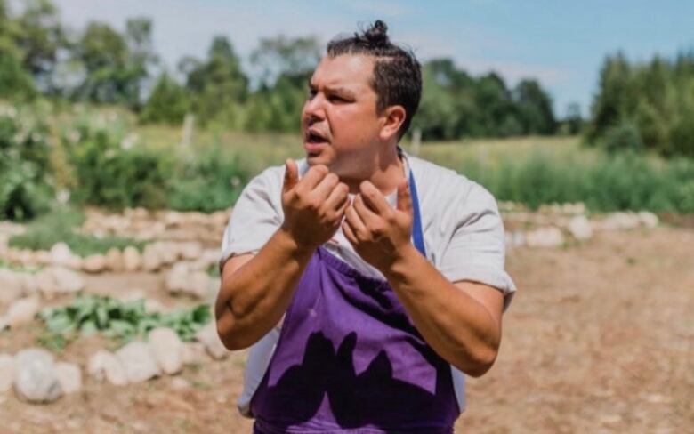 Man stands in field wearing apron.